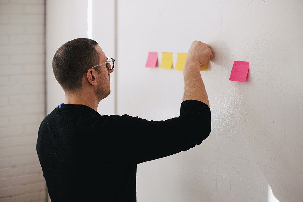 Mann klebt Post-It auf die Pinnwand